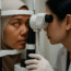 Ophthalmologist examining a Malay woman at a slit lamp; orange retinal reflex visible in a clean clinic.